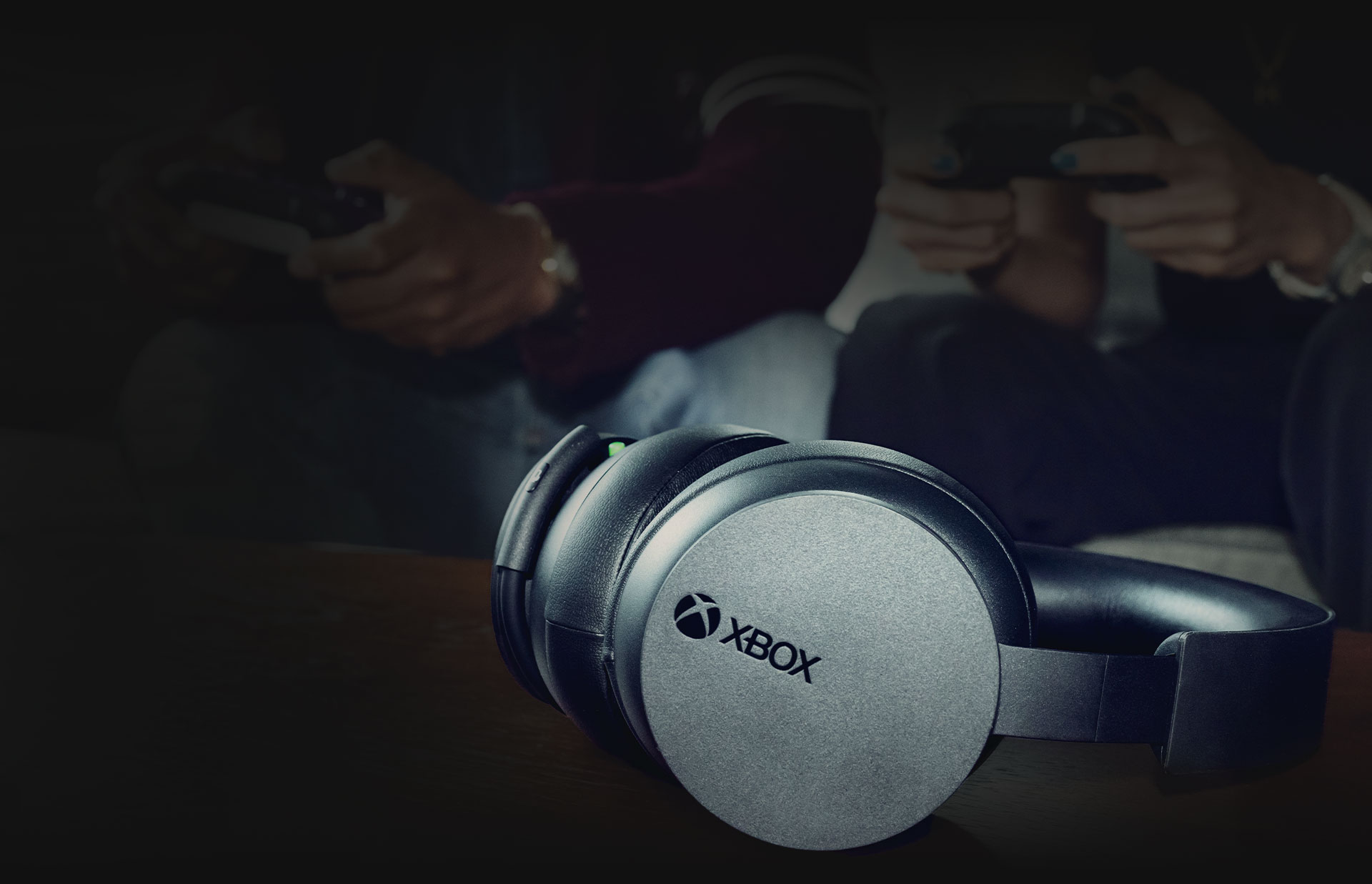 Xbox Wireless Headset on a table with two people holding controllers in the background
