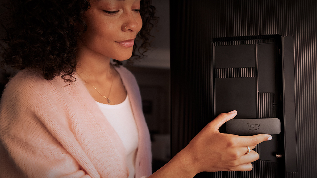 A woman plugging her Amazon Fire TV stick into the back of a TV